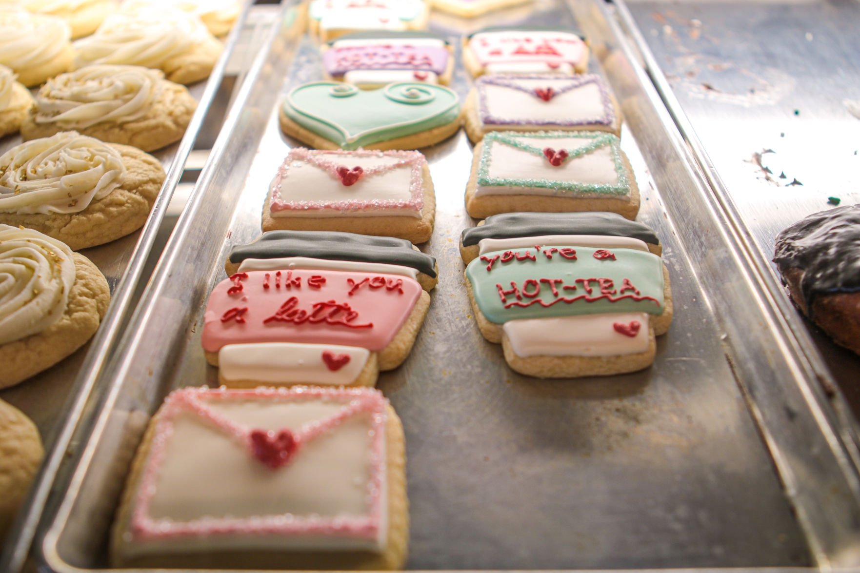 Two rows of iced cookies sit on a metal sheet in a baking case.